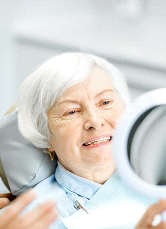 An older woman admiring her new smiles thanks to implant dentures in Jacksonville