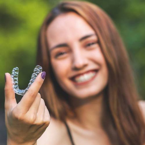 Woman outdoors smiling and holding an Invisalign tray