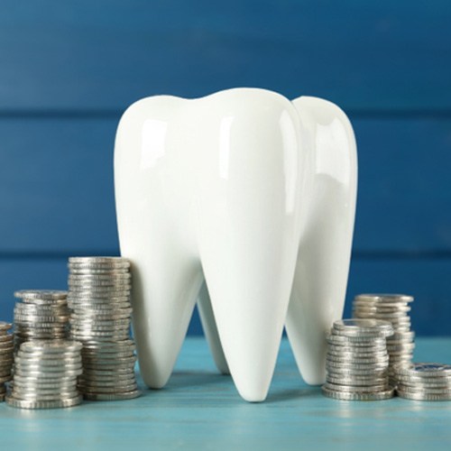 A ceramic model tooth and a stack of coins on a blue table