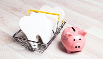 A pink piggy bank and fake teeth in a shopping basket on a light wooden background