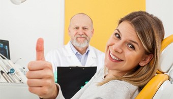 A smiling woman at a dentist’s office showing a thumbs up