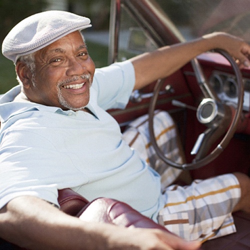 An older man driving a convertible and showing off his stellar smile after receiving dentures in Jacksonville