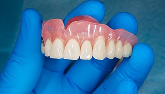 A close-up of an upper jaw denture held by a gloved hand