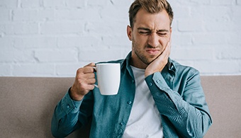 A man cupping his cheek as holds a mug