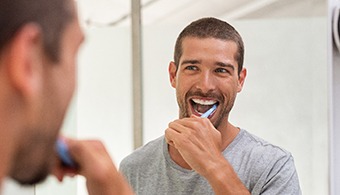 A happy man brushing his teeth in front of a bathroom mirror