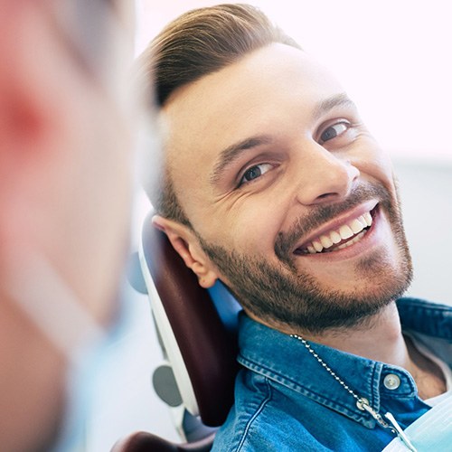 Man in denim shirt in dental chair smiling at dentist