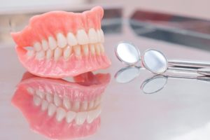 Set of dentures resting next to dental mirror on a reflective surface