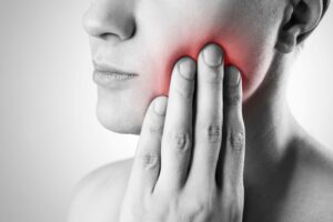 Greyscale nose to shoulder image of woman pressing her hand to her inflamed face