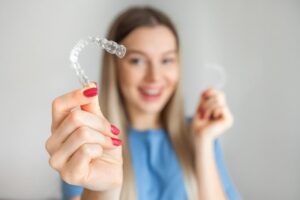 Woman holding clear aligner in foreground.