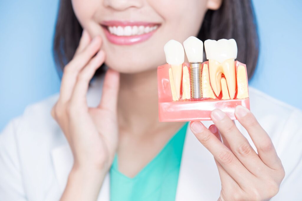 Dentist touching cheek with one hand holding model dental implant with other
