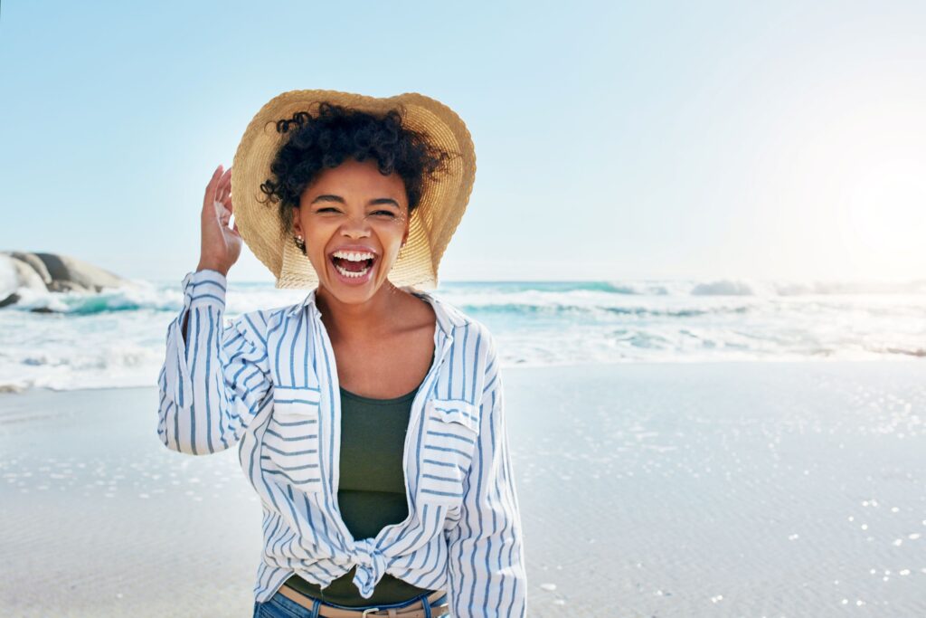 Woman at beach in striped shirt and straw hat laughing