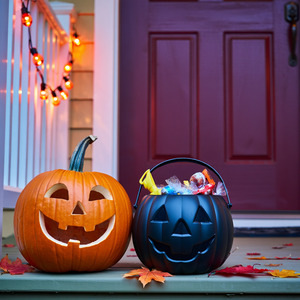 Jack-o-lantern sitting next to bucket of Halloween candy on porch